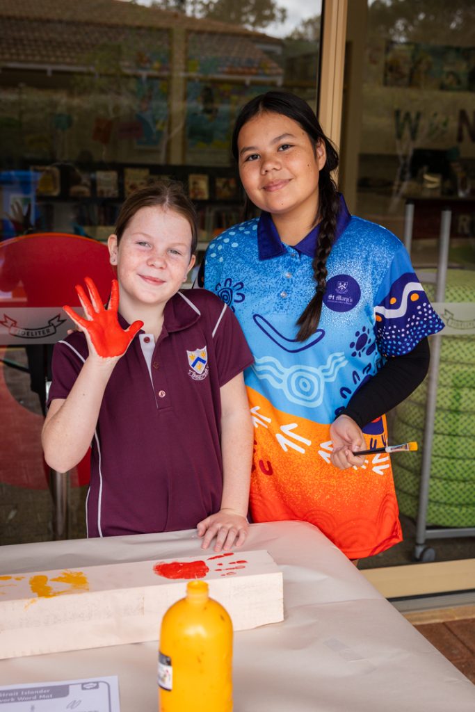 A Year 4 student with a red hand, ready to place a handprint on the wooden post