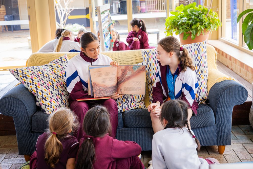 Junior School students sitting on the floor, actively engaged in the Dreamtime story being read to them by Senior School students