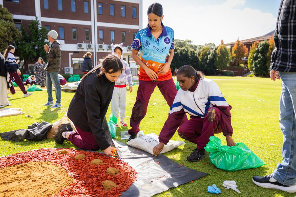 The girls working in the wind and rain to create this year's sand mural