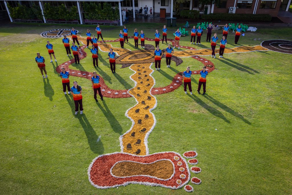 The students proudly standing around the completed sand mural.