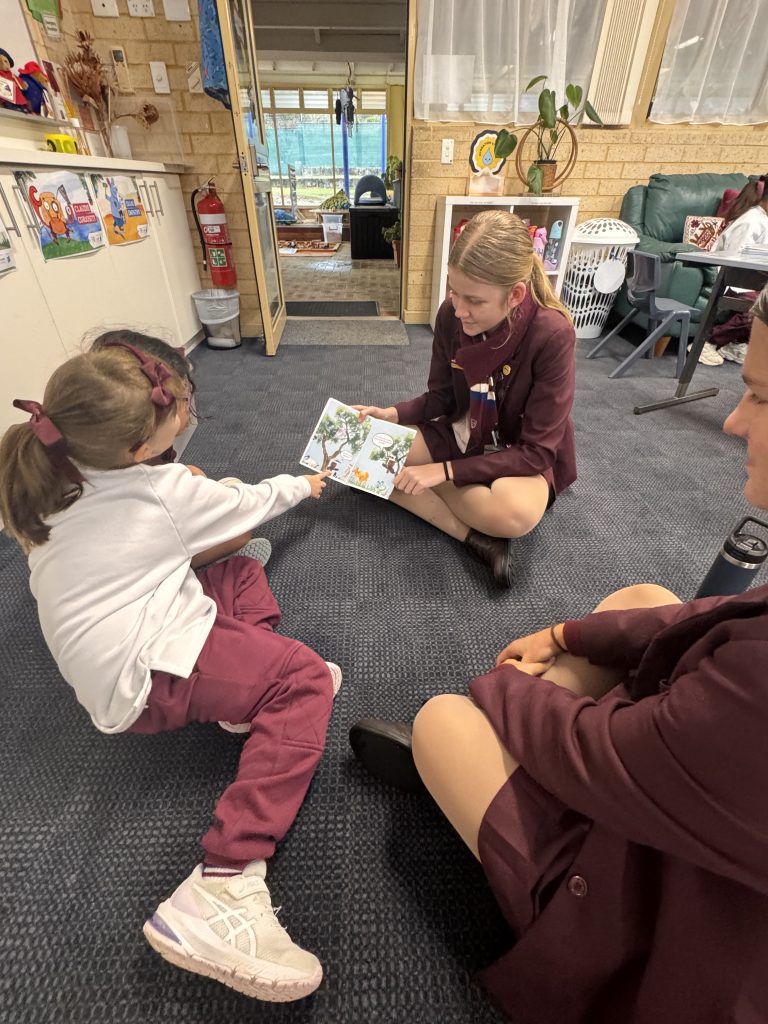 Year 1 students asking questions and pointing out illustrations in a book created by a Year 9 student