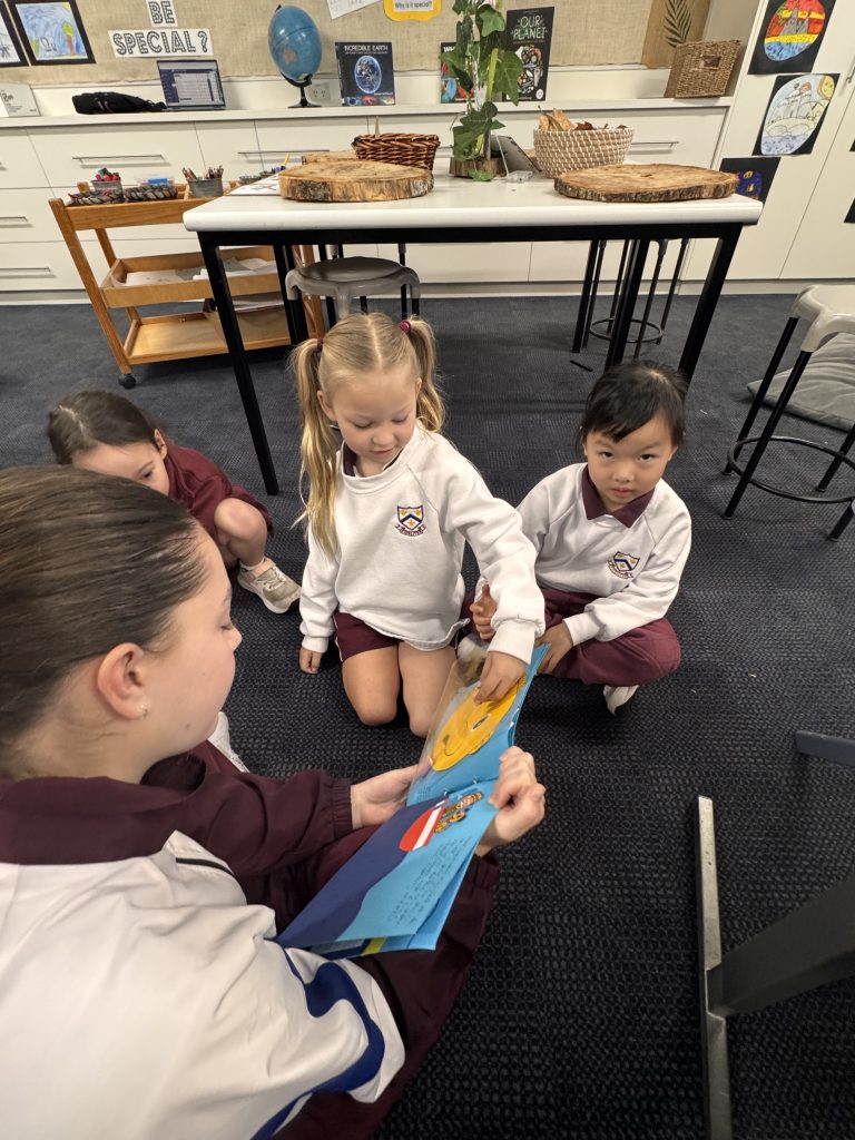 Year 1 students asking questions and pointing out illustrations in a book created by a Year 9 student
