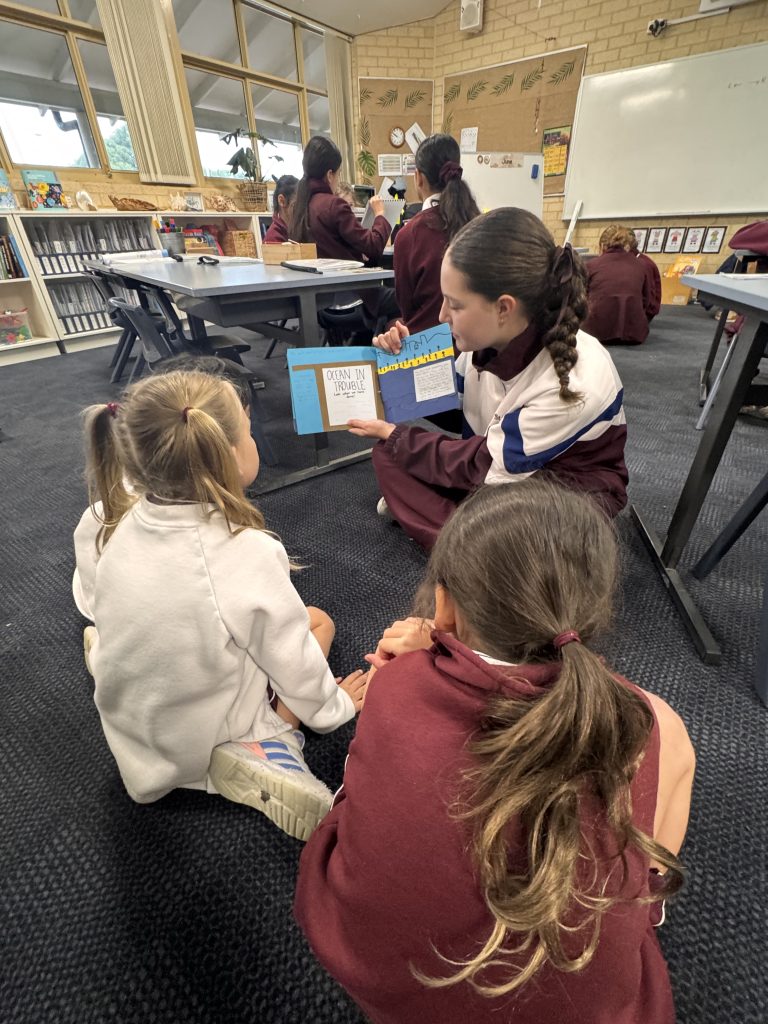 Year1 students listening intently while a Year 9 student reads their story